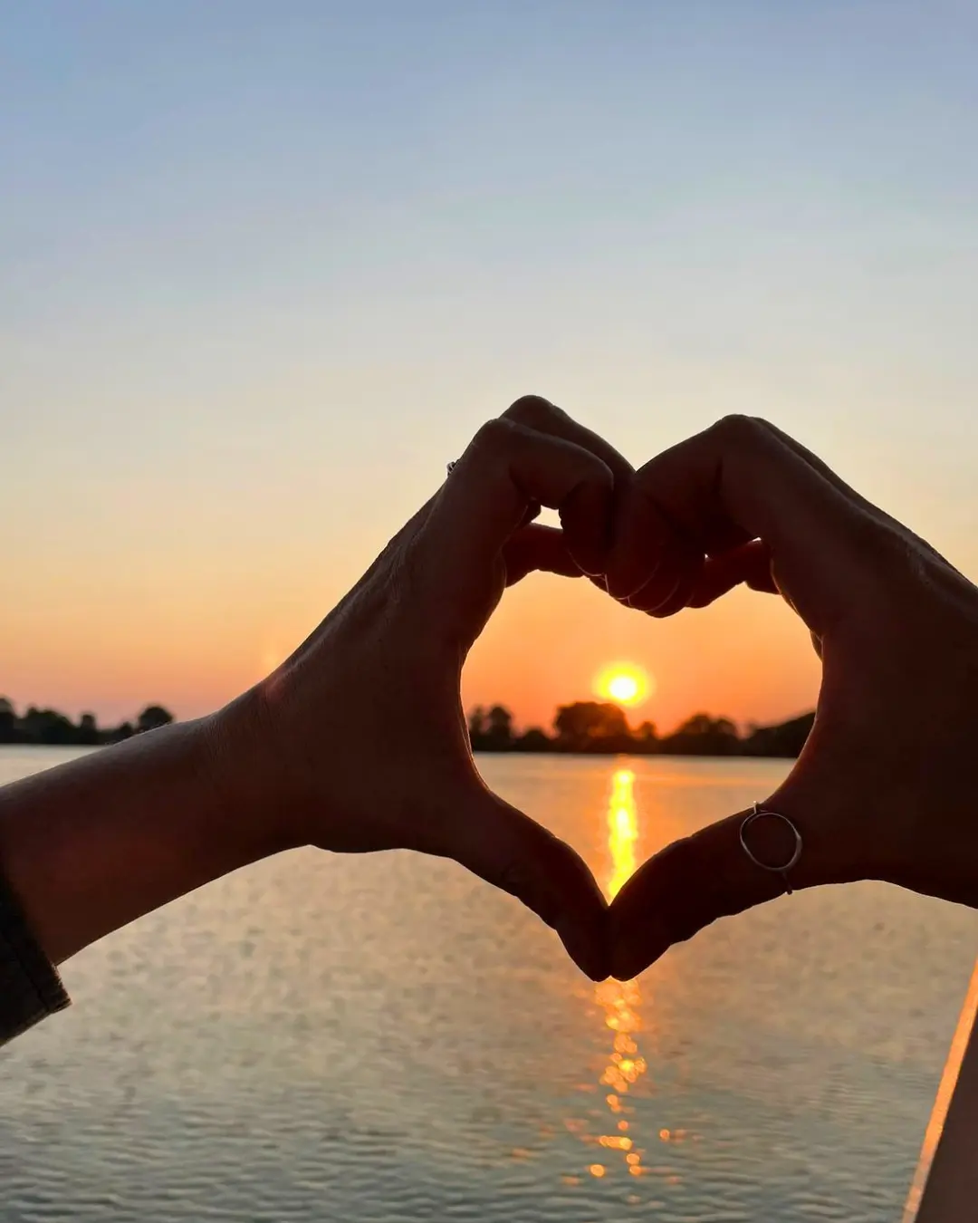 Hands making a heart shape around a sunset