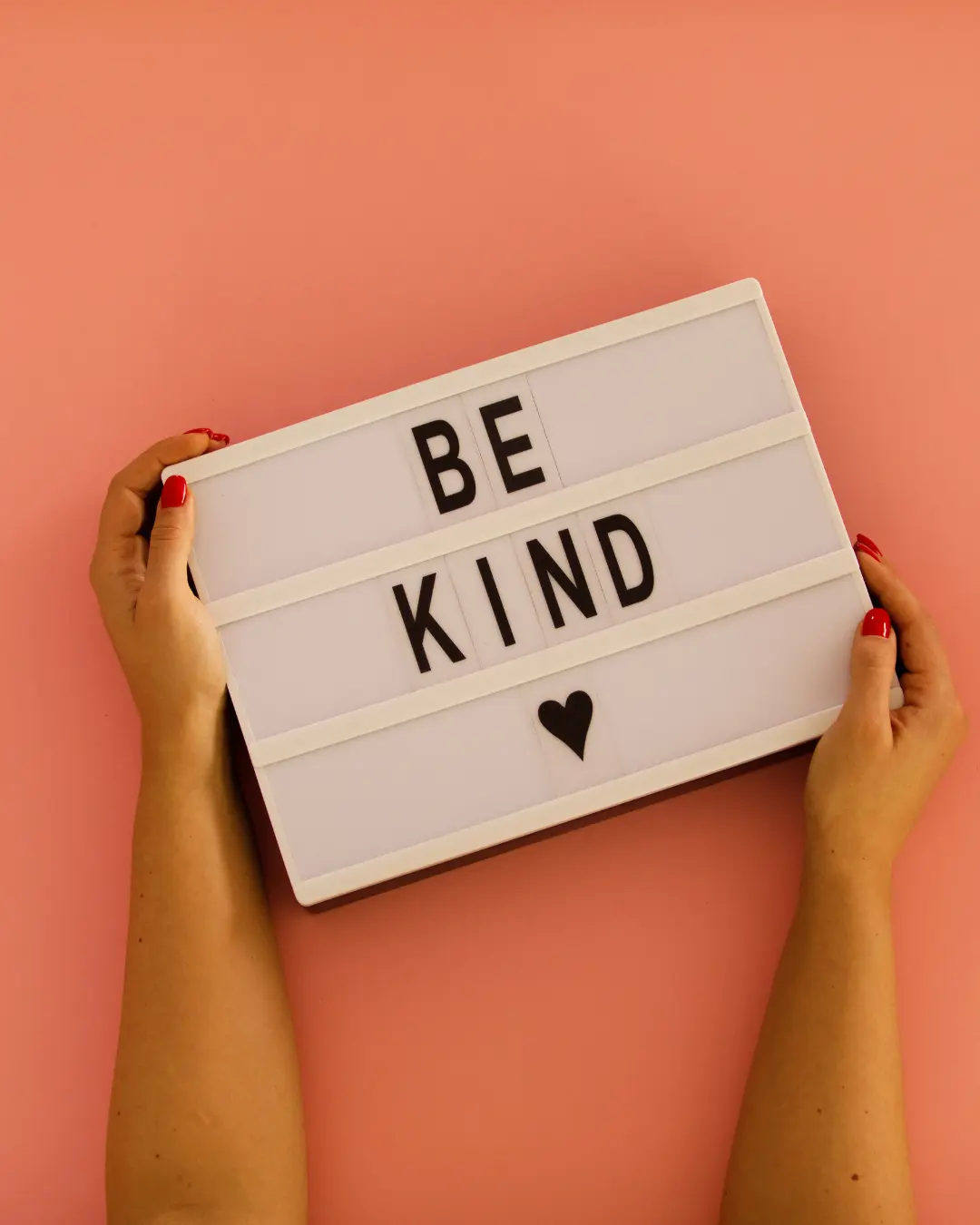 Hands holding a light box that reads Be Kind