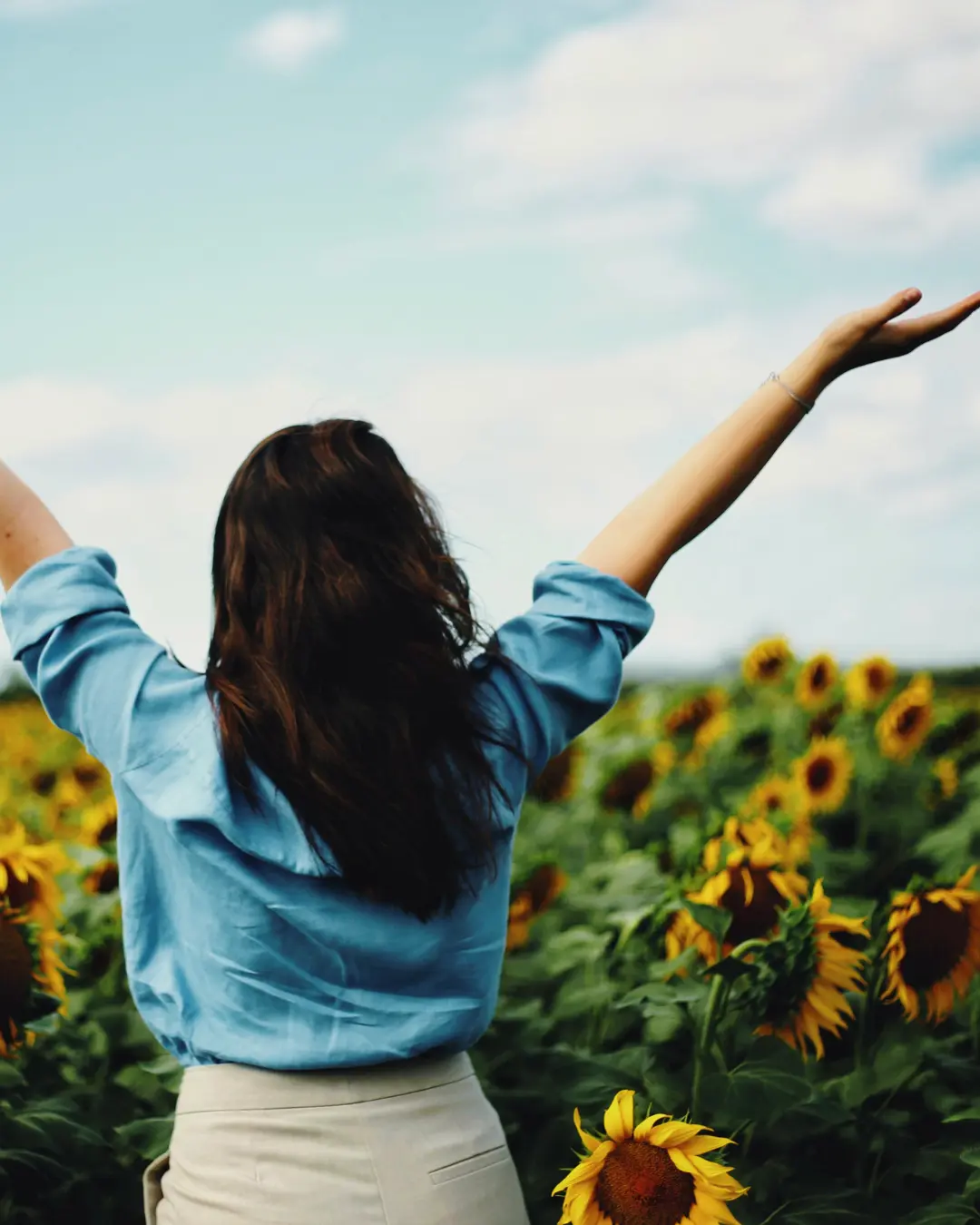 A woman standing joyfully in a field of sunflowers