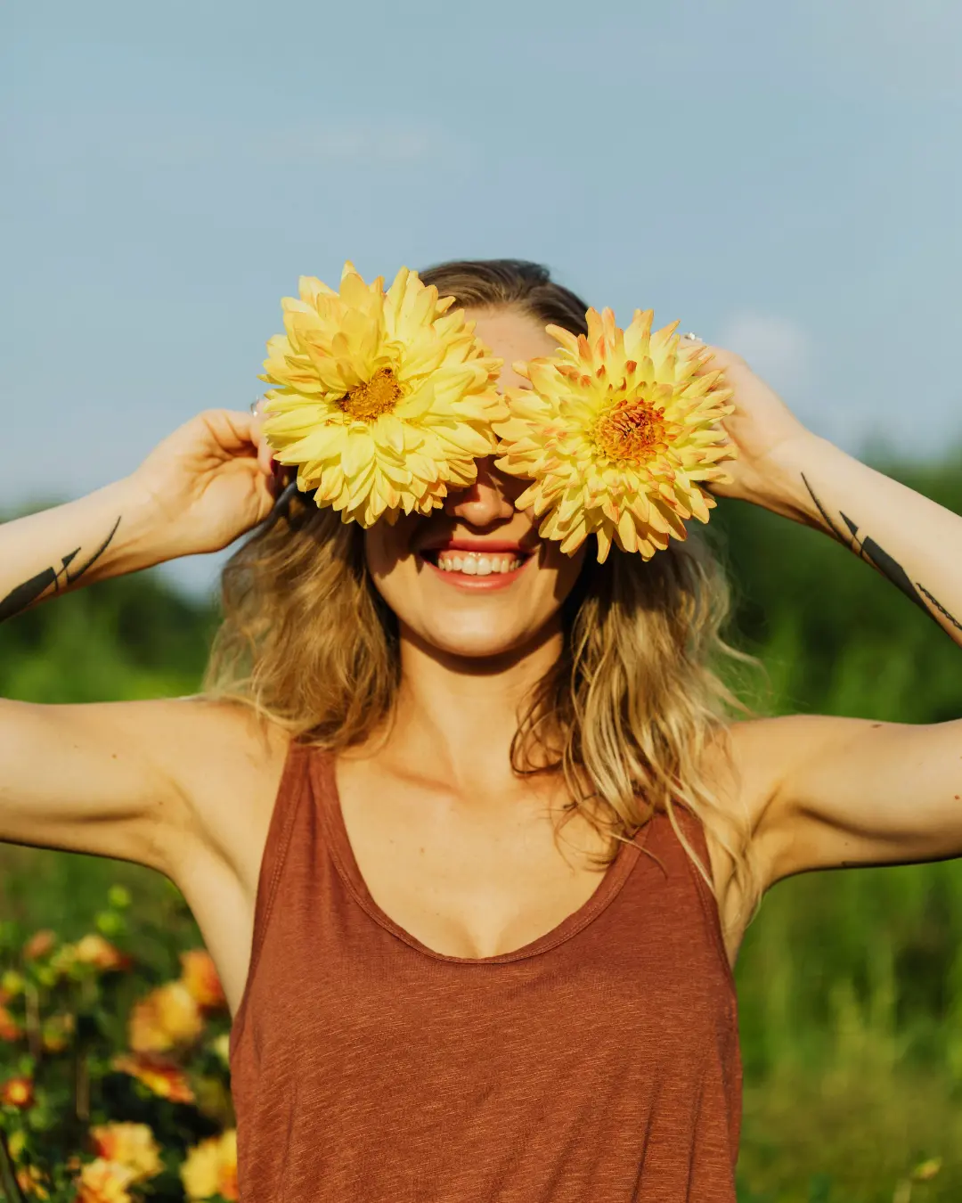 A woman playfully holding two yellow flowers over her eyes